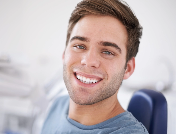 Young man with short brown hair smiling while seated in a dental chair.